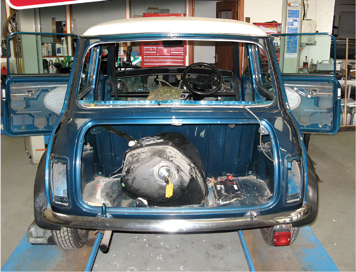 Classic Mini on ramps with the rear body panels removed, revealing the boot floor and inner structure as part of the strip down process.