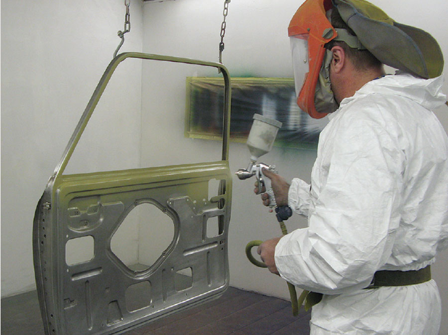 Professional spray booth with worker in protective gear painting a Mini shell.